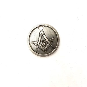 May include: Silver-toned metal pendant featuring a Masonic symbol, a compass and square with a 'G' in the center.