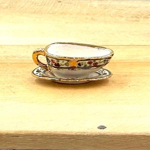May include: A small white porcelain teacup and saucer with a gold rim and floral pattern. The cup has a handle and the saucer has a scalloped edge.