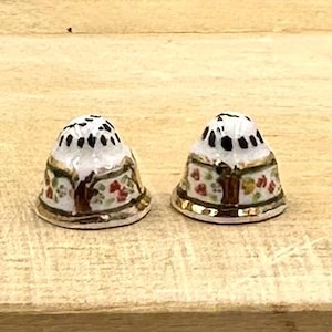 May include: Two white ceramic thimbles with gold trim and floral designs. The thimbles have black accents and red, yellow, and green flowers.