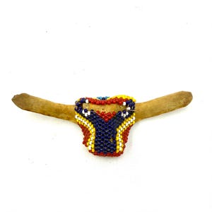 May include: A decorative piece featuring a light brown bone with a colorful beaded design. The beaded section is primarily red, blue, yellow, and white, creating a striking visual contrast against the bone.