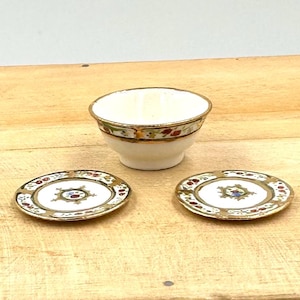 May include: A set of three miniature porcelain dishes with a white background and gold trim. The dishes have a floral pattern in red, blue, and green.