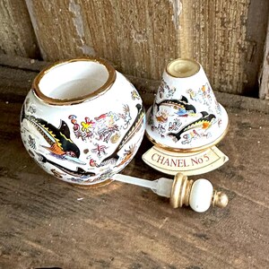 May include: A white ceramic perfume bottle and stopper set with gold trim. The bottle and lid are decorated with black, yellow, and orange sea creature illustrations. The label reads "CHANEL No 5".