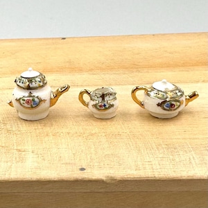 May include: A miniature porcelain tea set with gold trim and floral designs. The set includes a teapot, creamer, and sugar bowl.