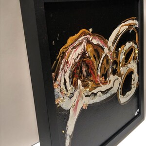 Puede incluir: Pintura abstracta en un marco negro con patrones de remolino dorados, blancos y rojos sobre un fondo negro. La pintura tiene una superficie texturizada con acentos de pan de oro.