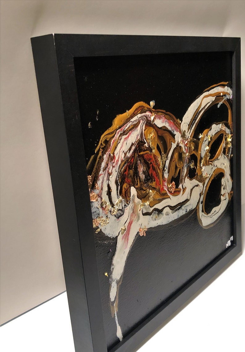 Puede incluir: Pintura abstracta en un marco negro con patrones de remolino dorados, blancos y rojos sobre un fondo negro. La pintura tiene una superficie texturizada con acentos de pan de oro.