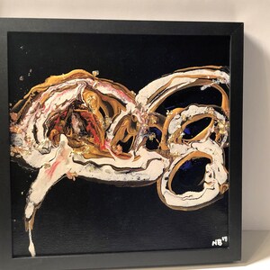 Puede incluir: Pintura abstracta con pintura dorada, blanca y azul sobre un fondo negro. La pintura est&aacute; enmarcada en negro.