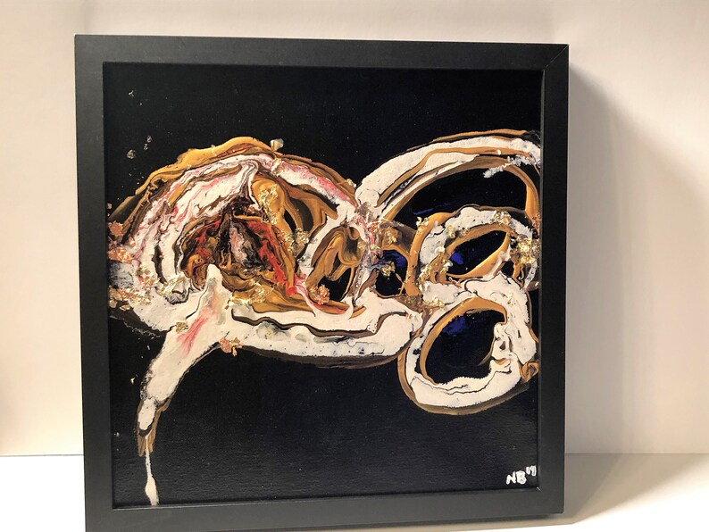 Puede incluir: Pintura abstracta con pintura dorada, blanca y azul sobre un fondo negro. La pintura est&aacute; enmarcada en negro.