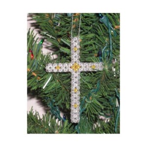 May include: A silver beaded cross ornament with gold accents hanging on a green Christmas tree.