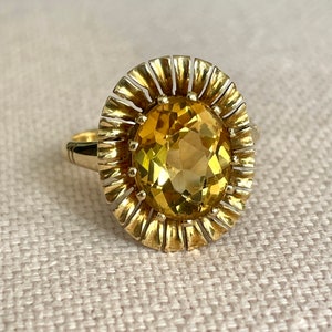 May include: A gold ring with a large, oval-shaped, yellow gemstone set in a sunburst design.