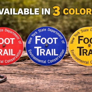 May include: Three circular signs with the text "FOOT TRAIL" are displayed. The signs are red, blue, and yellow, with the text in white and black. The signs also include the text "New York State Department of Environmental Conservation."
