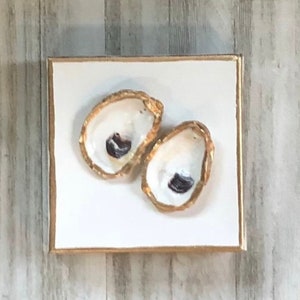 May include: Two gold-painted oyster shells with black interiors on a white background.