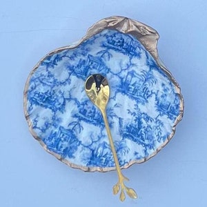 May include: A blue and white porcelain shell-shaped dish with a gold-colored spoon. The spoon has a leaf-shaped handle.