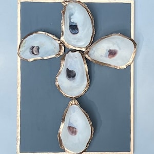 May include: Five oyster shells arranged in a cross shape on a gray background. The shells are painted gold and have a white interior.