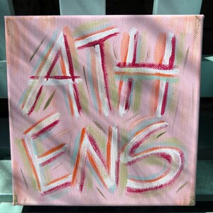 Peut inclure: Une peinture sur toile carr&eacute;e avec un fond rose clair pr&eacute;sentant le mot ATHENS peint en blanc, soulign&eacute; par des traits vibrants de magenta, d'orange et de vert clair. Le texte est superpos&eacute; sur un motif textur&eacute; de coups de pinceau multicolores.