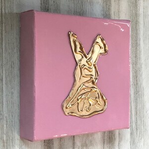 May include: A pink canvas painting with a gold metallic bunny rabbit silhouette.
