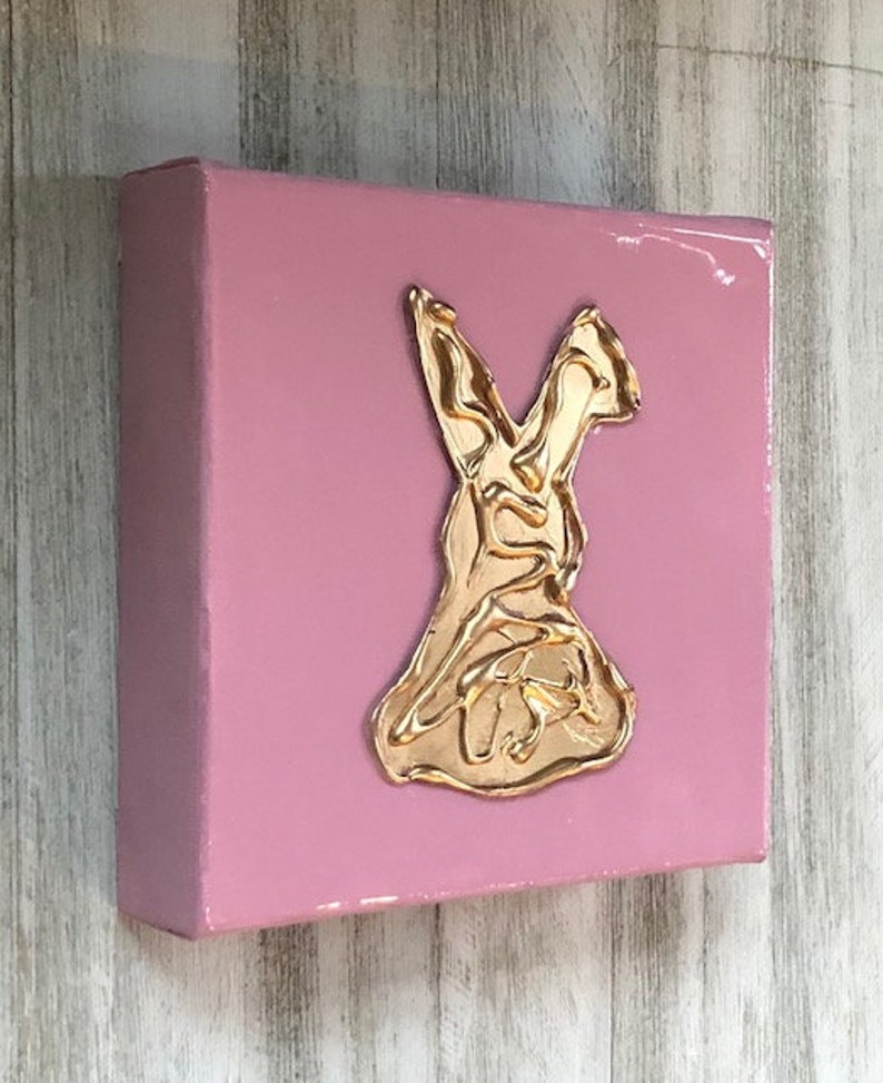 May include: A pink canvas painting with a gold metallic bunny rabbit silhouette.