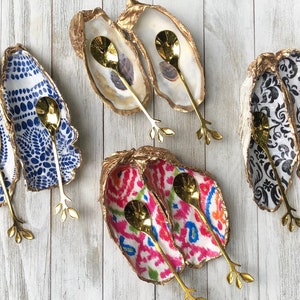 May include: Four sets of oyster shell dishes with gold-tone spoons. Each set features a different patterned design: blue and white, black and white, pink and white, and white with a natural shell finish.