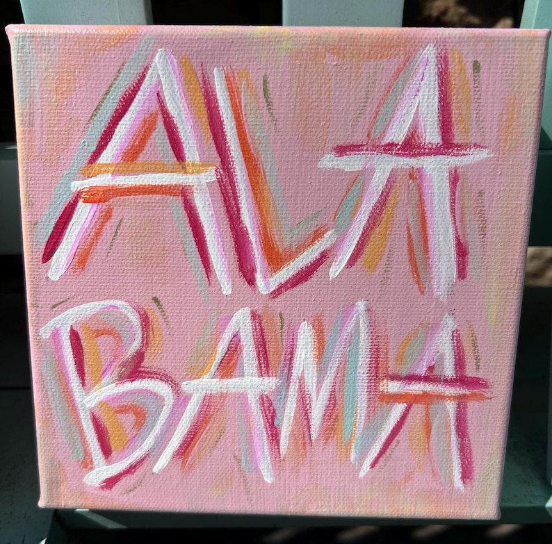 Peut inclure: Une peinture sur toile carr&eacute;e avec un fond rose clair pr&eacute;sentant le mot ALABAMA peint &agrave; la main dans un style expressif et superpos&eacute;. Les lettres sont r&eacute;alis&eacute;es avec des traits superpos&eacute;s de peinture blanche, rose vif et orange textur&eacute;e.