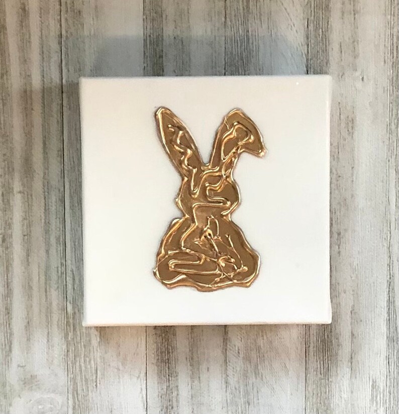 May include: A gold rabbit silhouette on a white canvas. The rabbit is made of a textured, raised material, giving it a 3D effect.