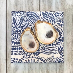 May include: Two gold-painted oyster shells on a white background with a blue paisley pattern.