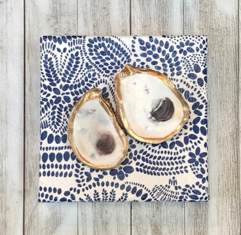 May include: Two gold-painted oyster shells on a white background with a blue paisley pattern.