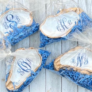 May include: Four white oyster shell dishes with gold trim and blue monograms. The dishes are packaged in clear plastic bags with blue tissue paper.