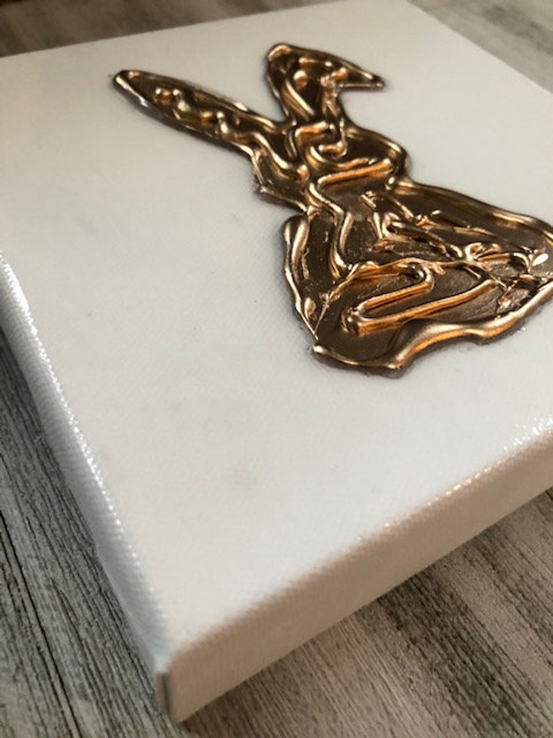 May include: A white canvas with a gold rabbit silhouette. The rabbit is made of raised, textured paint.