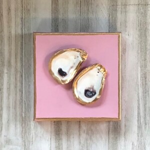 May include: Two gold-painted oyster shells on a pink background.