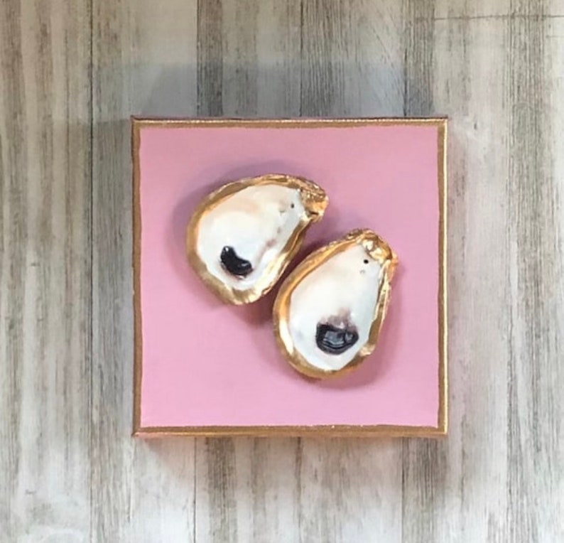 May include: Two gold-painted oyster shells on a pink background.