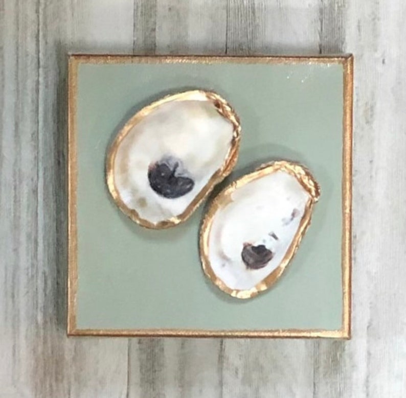 May include: Two oyster shells painted with gold leaf on a sage green background. The shells are arranged in a vertical orientation.