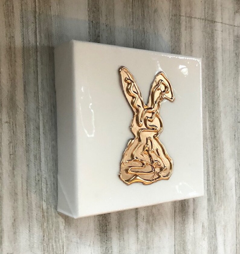 May include: A white canvas with a gold rabbit design. The rabbit is outlined in gold and is in a sitting position.