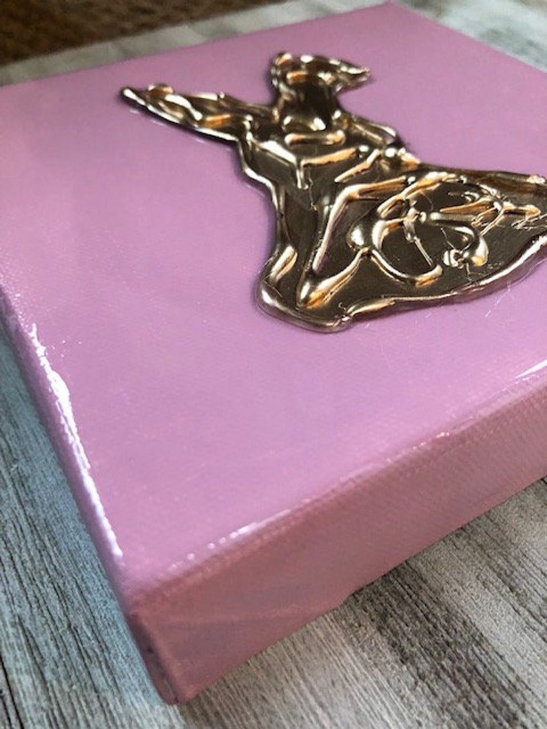 May include: A pink canvas with a gold-colored, three-dimensional sculpture of a woman in a flowing dress.