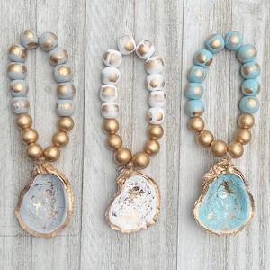 May include: Three strands of beaded garland with gold and white or blue beads. Each garland is attached to a white oyster shell with gold accents.