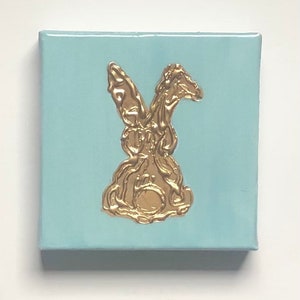 May include: A light blue canvas painting with a gold rabbit silhouette.