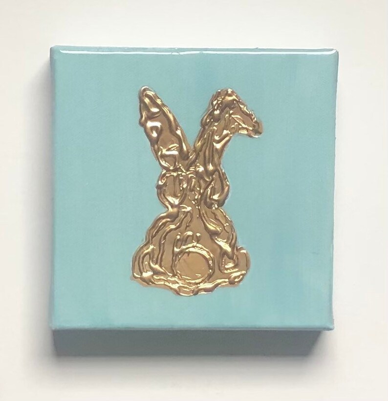 May include: A light blue canvas painting with a gold rabbit silhouette.