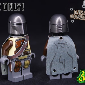 Puede incluir: Una minifigura LEGO gris que lleva una capa gris y un casco plateado. La minifigura est&aacute; etiquetada como "Galactic Gunslinger". El texto "CAPE ONLY!" est&aacute; en la esquina superior izquierda de la imagen. El texto "THE CAPE CANTINA" est&aacute; en la esquina inferior derecha de la imagen.