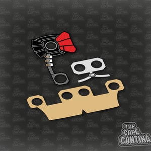 May include: A black and red toy blaster with a silver and gray toy helmet and a tan toy ship. The toy ship has a rounded top and a flat bottom. The toy blaster has a red handle and a black barrel. The toy helmet has two eye holes and a silver strap. The toy ship has a black outline.