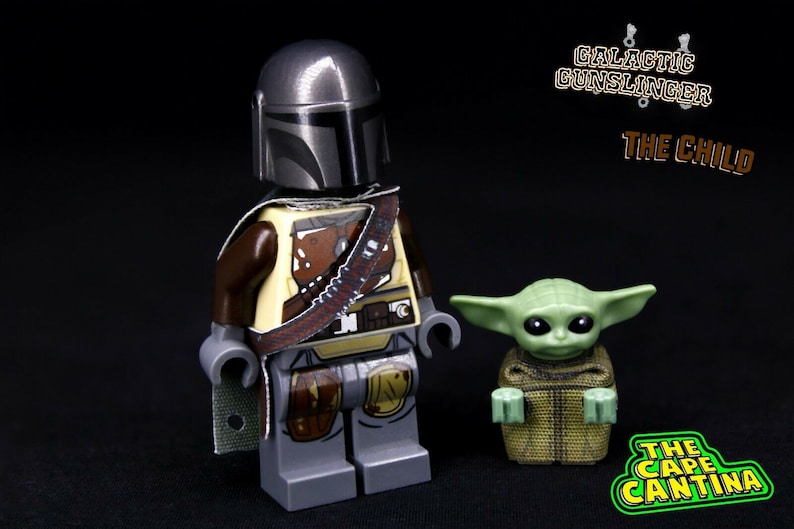 Puede incluir: Minifigura Lego del Mandaloriano de Star Wars, con una capa marr&oacute;n y gris y sosteniendo un rifle bl&aacute;ster. El Mandaloriano est&aacute; de pie junto a una minifigura Lego verde de The Child, tambi&eacute;n conocido como Baby Yoda.