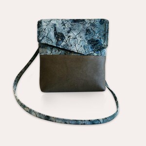 May include: A small blue and brown crossbody bag with a patterned flap and a long strap.
