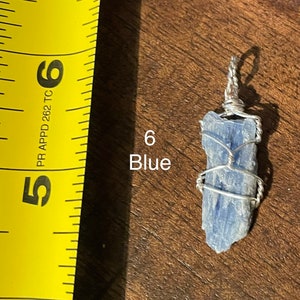 Peut inclure: Un cristal de kyanite bleu envelopp&eacute; de fil d'argent, suspendu &agrave; une cha&icirc;ne en argent. Le cristal mesure environ 5 cm de long. Le cristal est &eacute;tiquet&eacute; "6 Bleu".
