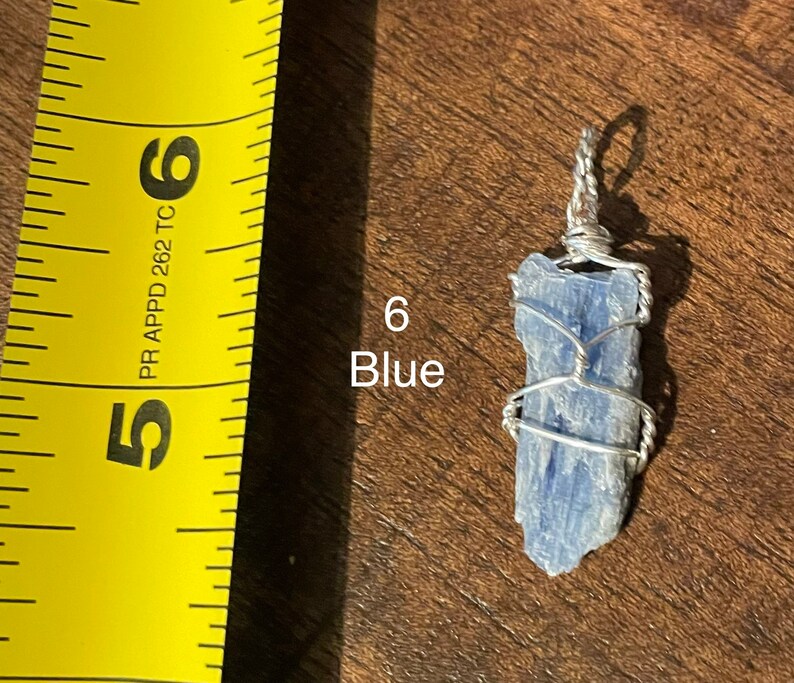 Peut inclure: Un cristal de kyanite bleu envelopp&eacute; de fil d'argent, suspendu &agrave; une cha&icirc;ne en argent. Le cristal mesure environ 5 cm de long. Le cristal est &eacute;tiquet&eacute; "6 Bleu".