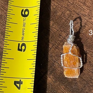 Peut inclure: Un pendentif en fil de fer avec un cristal naturel brun orang&eacute;. Le cristal mesure environ 3,8 cm de long et est envelopp&eacute; de fil d'argent. Le pendentif est suspendu &agrave; une cha&icirc;ne en argent.