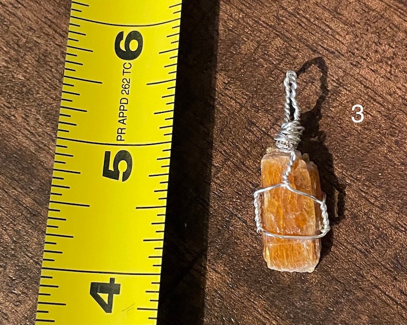 Peut inclure: Un pendentif en fil de fer avec un cristal naturel brun orang&eacute;. Le cristal mesure environ 3,8 cm de long et est envelopp&eacute; de fil d'argent. Le pendentif est suspendu &agrave; une cha&icirc;ne en argent.