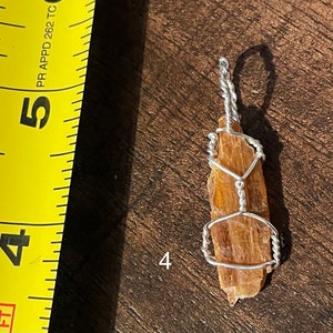 Peut inclure: Un pendentif en cristal brun et or envelopp&eacute; de fil d'argent. Le pendentif mesure environ 5 cm de long et est suspendu &agrave; une cha&icirc;ne en argent.