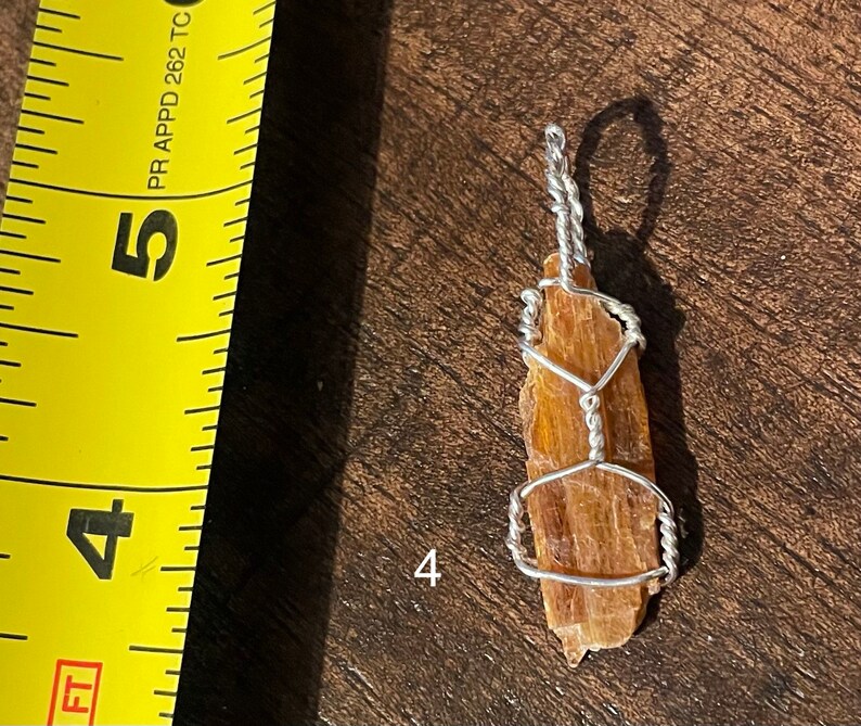 Peut inclure: Un pendentif en cristal brun et or envelopp&eacute; de fil d'argent. Le pendentif mesure environ 5 cm de long et est suspendu &agrave; une cha&icirc;ne en argent.