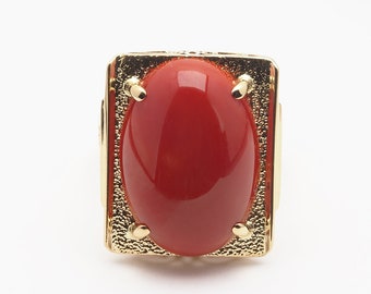 May include: A gold ring with a large, oval-shaped red coral gemstone set in a textured, rectangular frame.