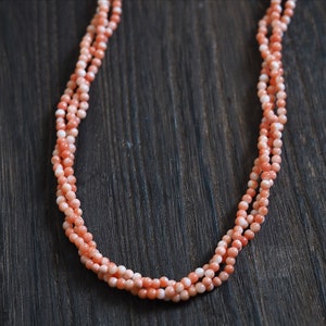 以下が含まれることがあります： 珊瑚のビーズでできたマルチストランドネックレス。ビーズは薄いピンク色で、滑らかで磨かれた仕上がりです。