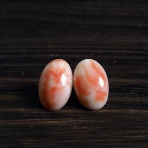 Puede incluir: Dos pendientes ovalados de coral con un patrón de mármol blanco y rosa.