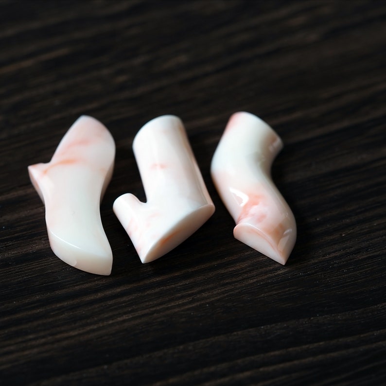 May include: Three coral-colored, smooth, polished, and organic-shaped pieces of coral. The coral is a light pink and white color.