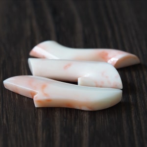 May include: Three pieces of coral in shades of white and pink, arranged in a curved shape on a dark wood surface.